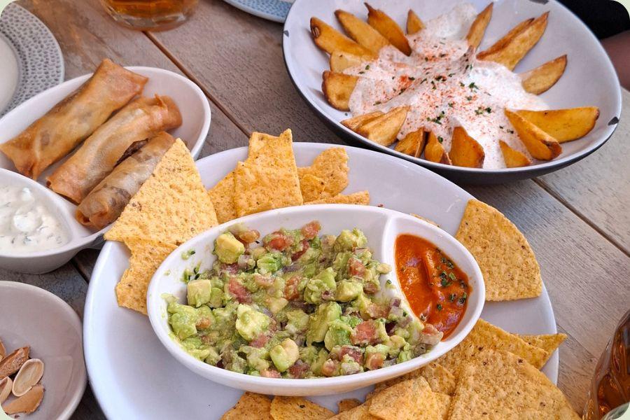 Een selectie van diverse Spaanse tapas op een houten tafel in Alicante, waaronder tortilla, gevulde broodjes, nacho's met guacamole en patatas bravas.