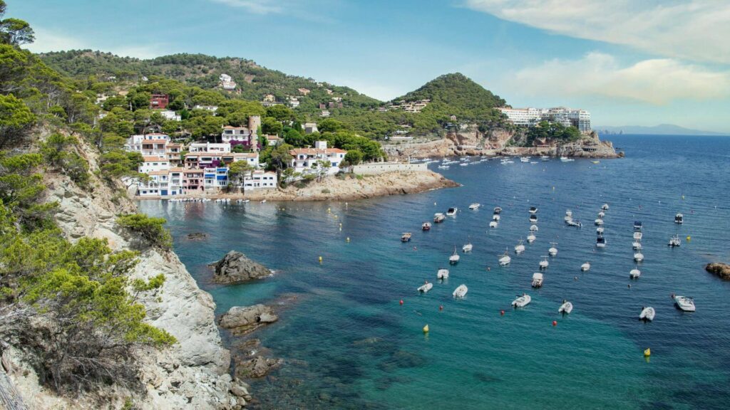 Kustlijn van de Costa Brava met turquoise water, kleurrijke huisjes en dobberende bootjes in een idyllische baai  
