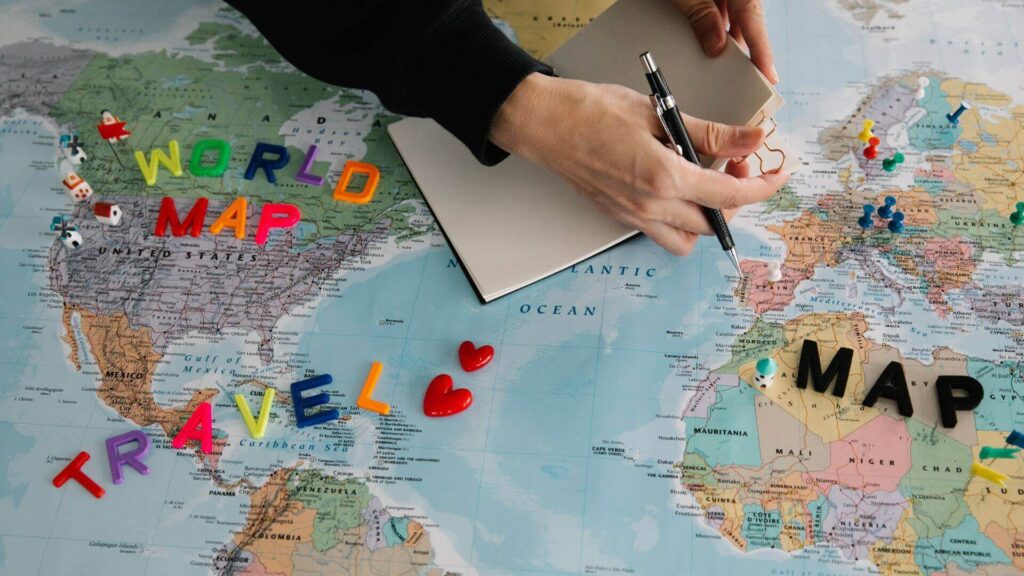 Reisbudget opstellen met wereldkaart, notitieboek en gekleurde pinnetjes ter voorbereiding op een vakantie.