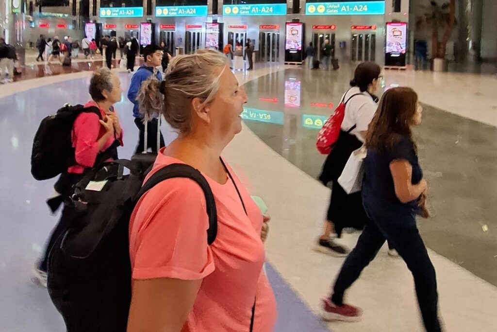 Solo reizen tips: backpacker loopt over het vliegveld van Dubai met rugzak en nekkussen