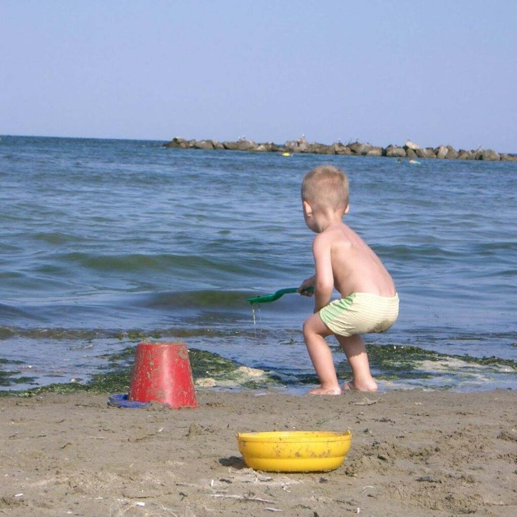 Jongentje speelt op het strand aan het Gardameer met water en zand
