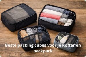 Bovenaanzicht van een set van vier opengevouwen zwarte en grijze packing cubes gevuld met opgerolde kleding en toiletartikelen, liggend op een houten vloer. Met de tekst: Beste packing cubes voor je koffer en backpack.