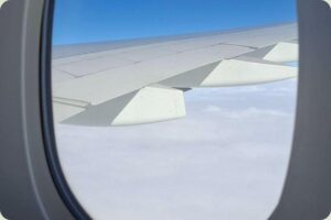 Uitzicht vanuit een vliegtuigraam op de vleugel en wolken, handig voor slim besparen op vliegtickets.