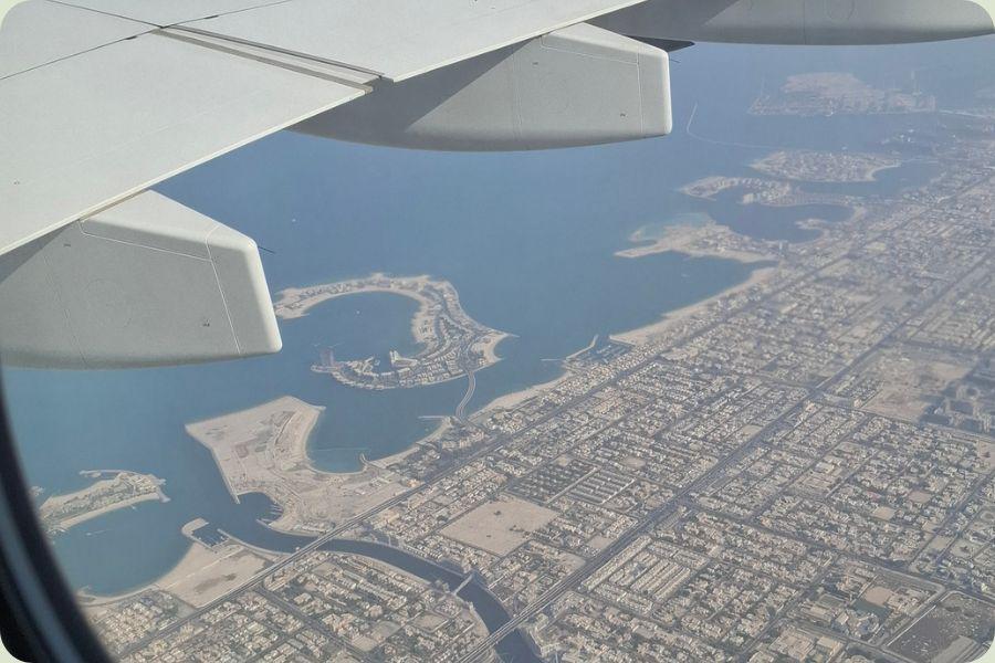 Luchtfoto vanuit een vliegtuigraam over een stad aan de kust, ideaal voor slim besparen op vliegtickets.