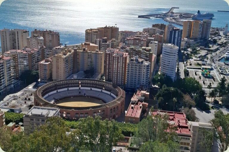 Panoramisch uitzicht over Málaga vanaf Gibralfaro met de ronde stierenvechtersarena Plaza de Toros de La Malagueta en de haven in de verte.