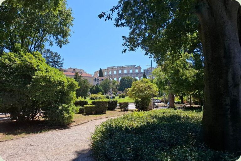 Een doorkijkje vanuit een groen park naar de historische Romeinse Arena in Pula