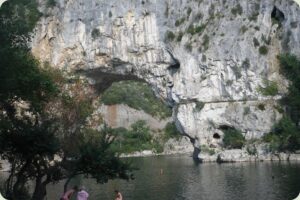 Grote natuurlijke rotsbrug Pont d'Arc over de rivier de Ardèche in Frankrijk, met beneden mensen op het strandje en in het water.