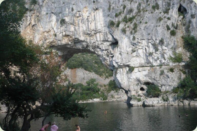 Grote natuurlijke rotsbrug Pont d'Arc over de rivier de Ardèche in Frankrijk, met beneden mensen op het strandje en in het water.